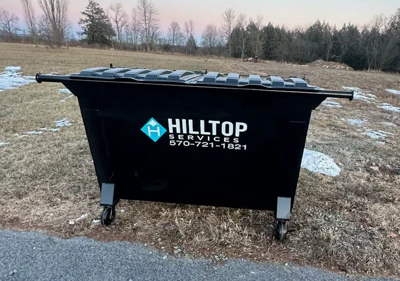 black dumper for residental trash pick up. Hilltop service logo on front